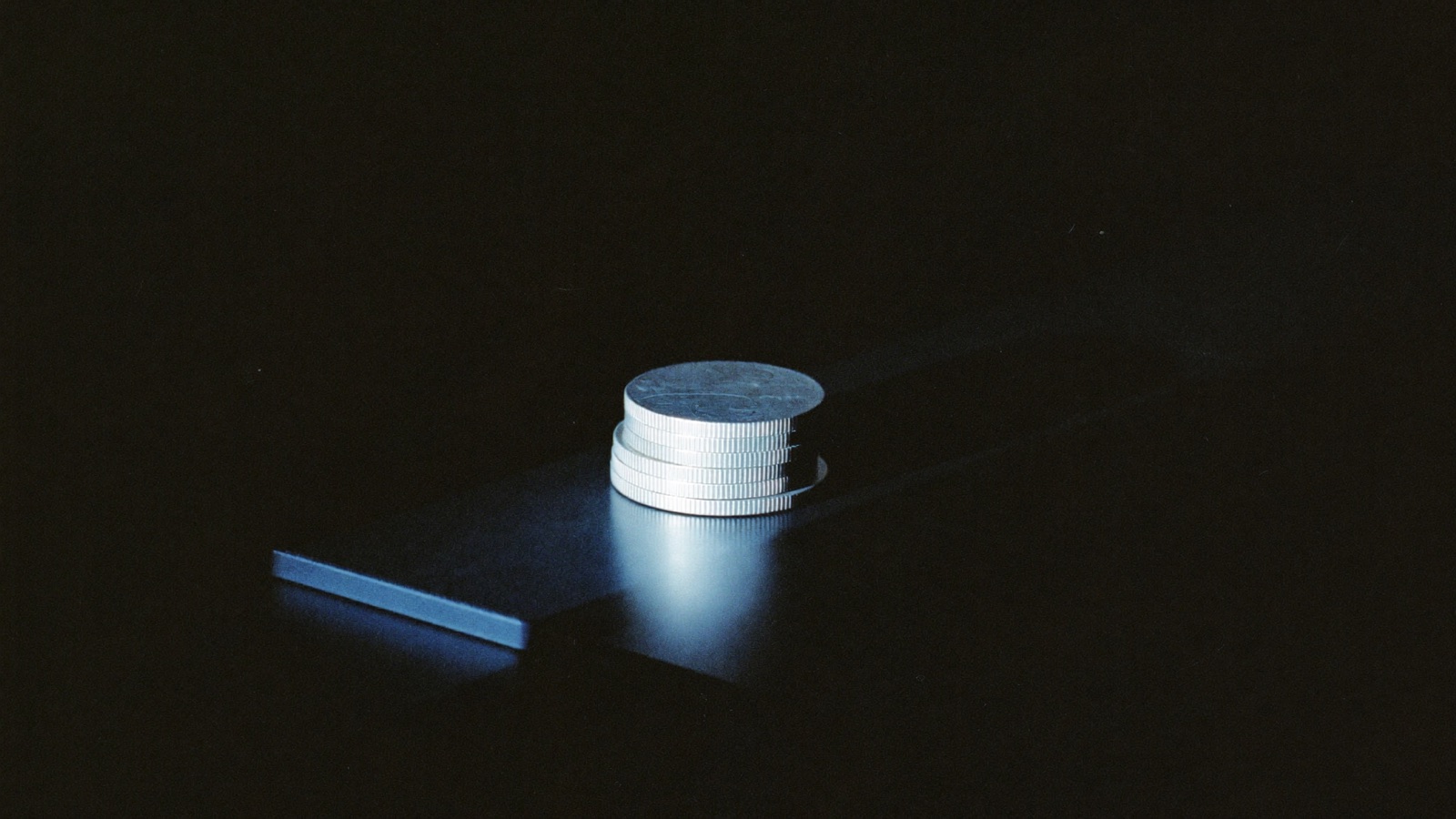 Pila de monedas iluminada por un haz de luz azul sobre fondo negro